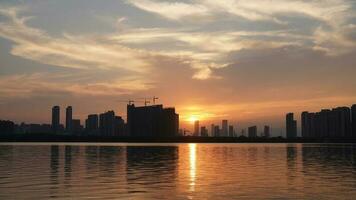 The beautiful sunset view with the buildings' silhouette and orange color sky mirrored in the peaceful lake in the city photo