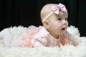 Beautiful baby girl in pink clothes on a black background. Baby at four months old. A funny child. photo