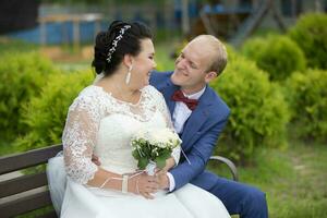 The fat bride and the thin groom sit on the bench and talk to each other. photo