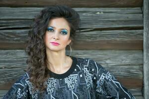 Portrait of a brunette woman with bright makeup who stands against a background of a wooden wall. photo