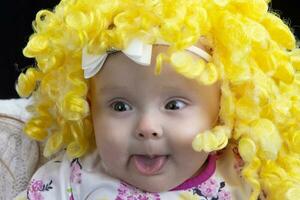 A funny little baby in a yellow wig shows her tongue. photo