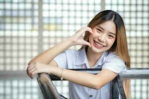 Beautiful young Asian student girl wearing a Thai university uniform and teething retainer stands smiling cutely in the building during free time while waiting for class. photo