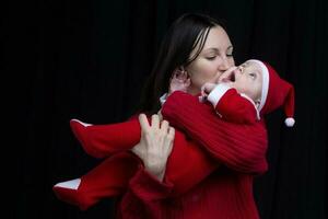 mamá y pequeño niño a Navidad. un mujer sostiene su hijo en su brazos, quien es vestido en Papa Noel claus ropa. foto