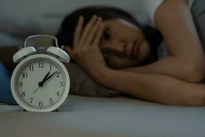 asiático mujer en cama tarde molesto a dormir sufrimiento insomnio, insomne o asustado en un pesadilla, mirando triste preocupado y estresado. cansado y dolor de cabeza o migraña despertar arriba en el medio de el noche. foto