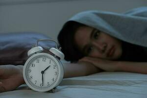 asian woman in bed late trying to sleep suffering insomnia, sleepless or scared in a nightmare, looking sad worried and stressed. Tired and headache or migraine waking up in the middle of the night. photo