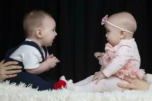 Funny little boy and girl are sitting opposite each other. Brother and sister kids. Children under one year old. photo