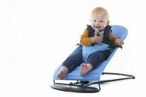 A cute toddler sits in a baby lounger and smiles on a white background. A beautiful one-year-old child. photo