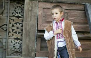 pequeño chico en eslavo nacional ropa en un de madera antecedentes. bielorruso o ucranio niño en un bordado camisa. foto