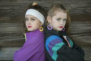 Little girls in bright clothes with makeup on their faces on a wooden background. A child in the style of the nineties. photo