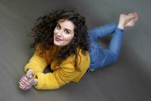 A dark-haired girl in jeans lies on the floor and looks at the camera. Beautiful brunette. photo