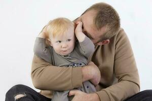 en contra un gris fondo, papá suavemente Besos su un año de edad hijo. padre y pequeño hijo. foto