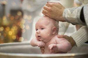 Orthodox baptism of a child.Baby in the baptismal font in the church. The hands of the priest pour water on the child during the ceremony of accepting faith. photo