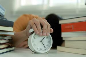 un estudiante asiático apaga el despertador porque está cansado de leer, el hombre se prepara para el examen y aprende lecciones en la biblioteca. estrés, desesperación, prisa, incomprensión de la lectura, desánimo. foto