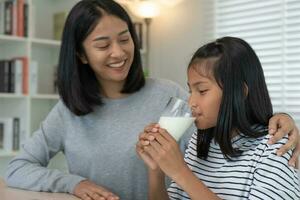 Asian young little girl learn at home. Do homework with kind mother help, encourage for exam. Mom pass on a glass of milk to daughter. Girl happy Homeschool. Mom teach and advice education together. photo