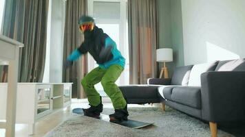 Spaß Video. Mann gekleidet wie ein Snowboarder Fahrten ein Snowboard auf ein Teppich im ein gemütlich Zimmer. warten zum ein schneebedeckt Winter video