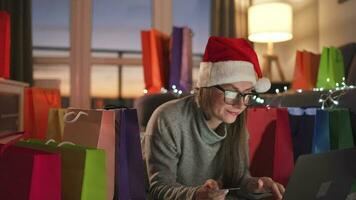 content femme avec des lunettes portant une Père Noël claus chapeau est mensonge sur le tapis et fait du un en ligne achat en utilisant une crédit carte video