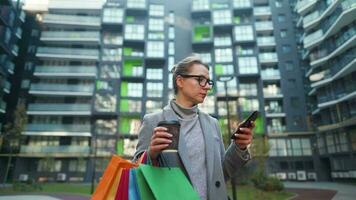 mulher caminhando em uma o negócio distrito detém Leve embora café compras bolsas e usa Smartphone video