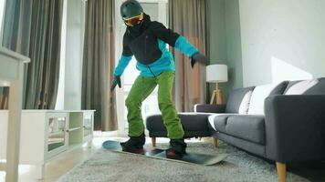 Fun video. Man dressed as a snowboarder rides a snowboard on a carpet in a cozy room. Waiting for a snowy winter video