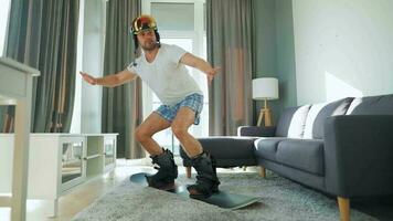 Fun video. Man in shorts and a T-shirt depicts snowboarding on a carpet in a cozy room. Waiting for a snowy winter video