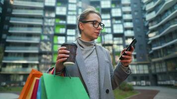 mulher caminhando em uma o negócio distrito detém Leve embora café compras bolsas e usa Smartphone video