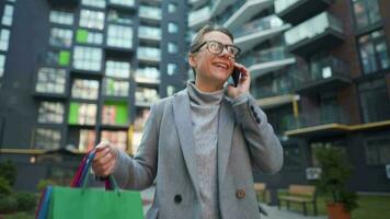 mujer caminando en un negocio distrito con compras pantalones y hablando en el teléfono inteligente urbano estilo de vida y digital video