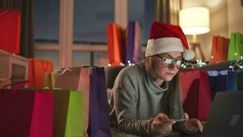 content femme avec des lunettes portant une Père Noël claus chapeau est mensonge sur le tapis et fait du un en ligne achat en utilisant une crédit carte video