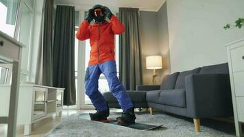 Fun video. Man dressed as a snowboarder rides a snowboard on a carpet in a cozy room. Waiting for a snowy winter video