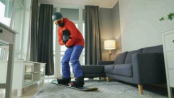 Fun video. Man dressed as a snowboarder rides a snowboard on a carpet in a cozy room. Waiting for a snowy winter video