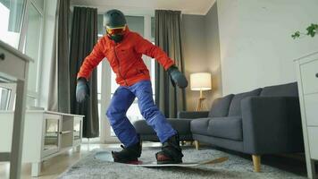 Fun video. Man dressed as a snowboarder rides a snowboard on a carpet in a cozy room. Waiting for a snowy winter video