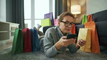 Happy woman is lying on the floor and makes an online purchase using a credit card and smartphone. Shopping bags around video