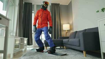 Fun video. Man dressed as a snowboarder rides a snowboard on a carpet in a cozy room. Waiting for a snowy winter video