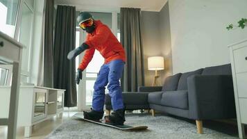 amusement vidéo. homme habillé comme une snowboarder monte une snowboard sur une tapis dans une confortable chambre. attendre pour une neigeux hiver video