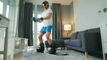 Fun video. Man in shorts and a T-shirt depicts snowboarding on a carpet in a cozy room. Waiting for a snowy winter video