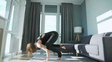 Young caucasian woman in black jumpsuit doing handstand bakasana at home to develop power, flexibility and balance video