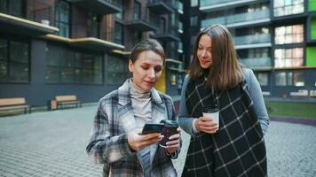 deux content femmes en marchant avec à emporter café et parlant avec l'intérêt parmi se dans le affaires district. lent video