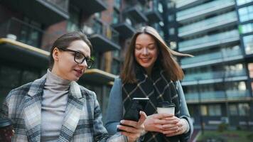 två Lycklig kvinnor gående med hämtmat kaffe och talande med intressera bland sig själva i de företag distrikt. långsam video