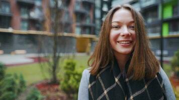 Porträt von ein Herrlich dunkel behaart Frau lächelnd charmant während Stehen gegen das Hintergrund von modern Gebäude video