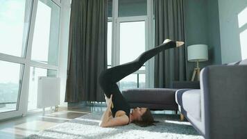 Young caucasian woman in black jumpsuit doing yoga at home to develop flexibility and balance. Slow motion video