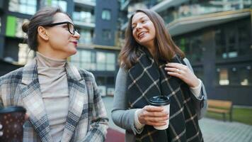 dos contento mujer caminando con para llevar café y hablando con interesar entre sí mismos en el negocio distrito. lento movimiento video