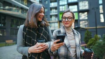 zwei glücklich Frauen Gehen mit wegbringen Kaffee und reden mit Interesse unter sich im das Geschäft Bezirk. schleppend video