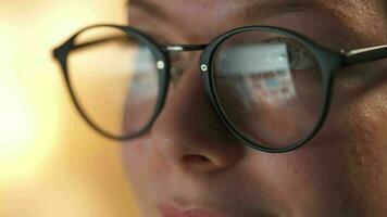 mujer en lentes mirando en el monitor y surf Internet a noche. el monitor pantalla es reflejado en el lentes. trabajo a noche. hogar oficina. remoto trabajo video