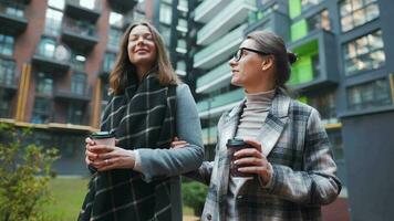 zwei glücklich Frauen Gehen mit wegbringen Kaffee und reden mit Interesse unter sich im das Geschäft Bezirk. schleppend Bewegung video