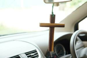 Closeup wooden crucifix hang in front steering wheel and console of the car. Concept, talisman,amulet to prevent accidents. Belief, faith,holy in god to protect when driving. photo