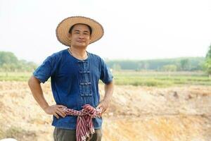 Handsome Asian man farmer wears hat, blue shirt, pose hands on waist, feel confident. Concept , Agriculture occupation. Thai Farmer . photo