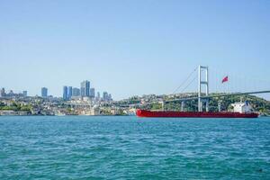 A cargo ship sails under a bridge in Istanbul on a summer and sunny day. photo
