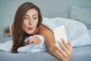 Brunette woman on bed with phone photo