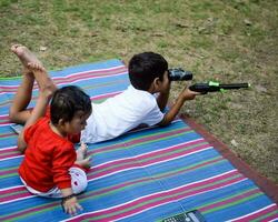 dos contento Niños en sociedad parque, contento asiático hermanos quien son sonriente felizmente juntos. hermanos jugar al aire libre en verano, mejor amigos. niñito bebé chico jugando con su contento hermano en el jardín foto