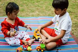 dos contento Niños en sociedad parque, contento asiático hermanos quien son sonriente felizmente juntos. hermanos jugar al aire libre en verano, mejor amigos. niñito bebé chico jugando con su contento hermano en el jardín foto