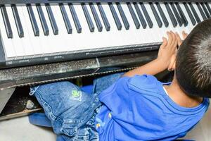 asiático chico jugando el sintetizador o piano. linda pequeño niño aprendizaje cómo a jugar piano. niño manos en el teclado interior. foto