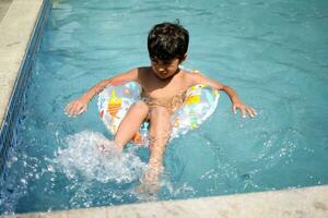 Happy Indian boy swimming in a pool, Kid wearing swimming costume along with air tube during hot summer vacations, Children boy in big swimming pool. photo